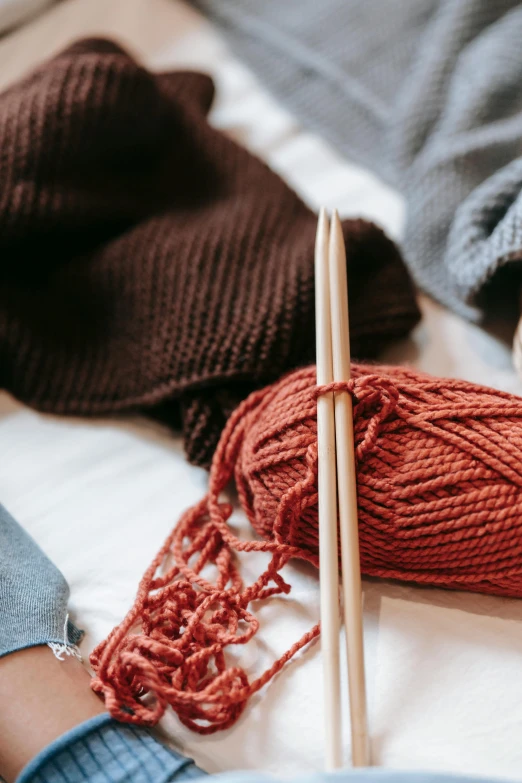 a person laying on a bed with yarn and knitting needles, unsplash, brown red blue, cotton fabric, beanie, school class