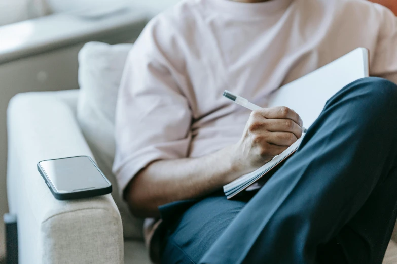 a man sitting on a couch holding a pen and paper, a drawing, trending on pexels, writing on a clipboard, lachlan bailey, thumbnail, high resolution image