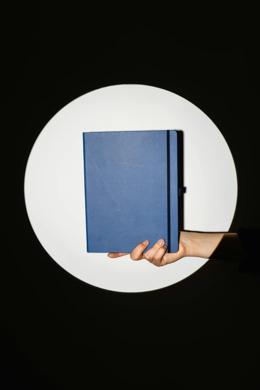 a person holding a blue book in their hand, by Doug Ohlson, trending on unsplash, bauhaus, half moon, ignant, spotlight, navy-blue