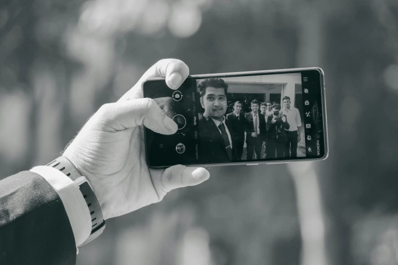 a person taking a picture with a cell phone, a black and white photo, by Alejandro Obregón, pexels contest winner, realism, wedding, selfie!!!!! of a man, holding it out to the camera, android phones