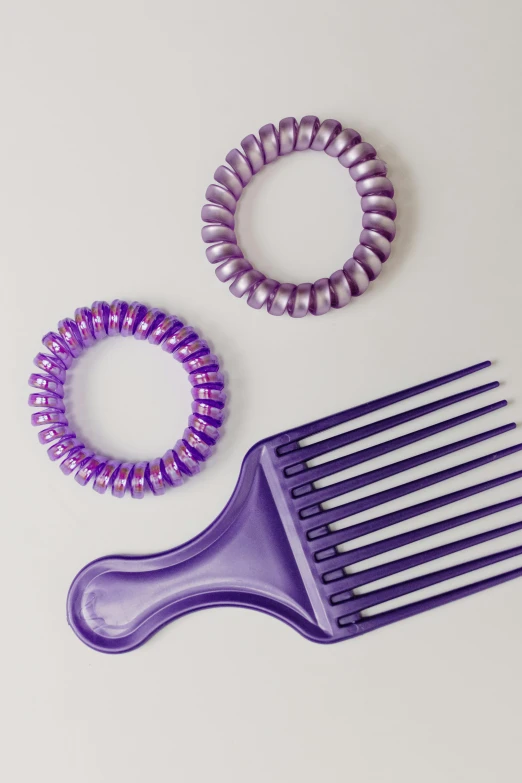 two purple hair ties and a comb on a white surface, inspired by An Gyeon, glossy plastic, spiral, late 1 9 6 0's, ((purple))