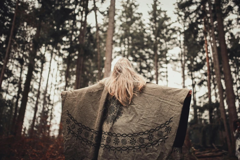 a woman standing in the woods with a blanket, by Anna Boch, pexels contest winner, renaissance, over the shoulder view, hippie fashion, throw, scandinavian / norse influenced