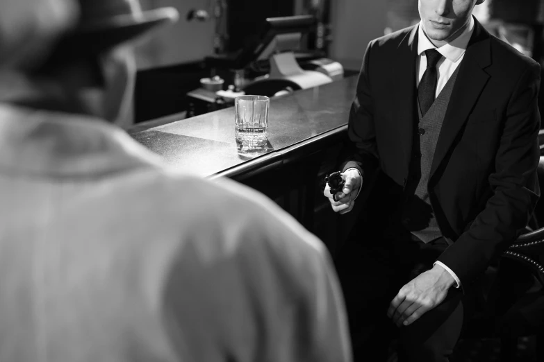 a man in a suit standing in front of a bar, a black and white photo, by Maurycy Gottlieb, pexels, purism, bank robbery movies, drinking a martini, two men in black, spying discretly