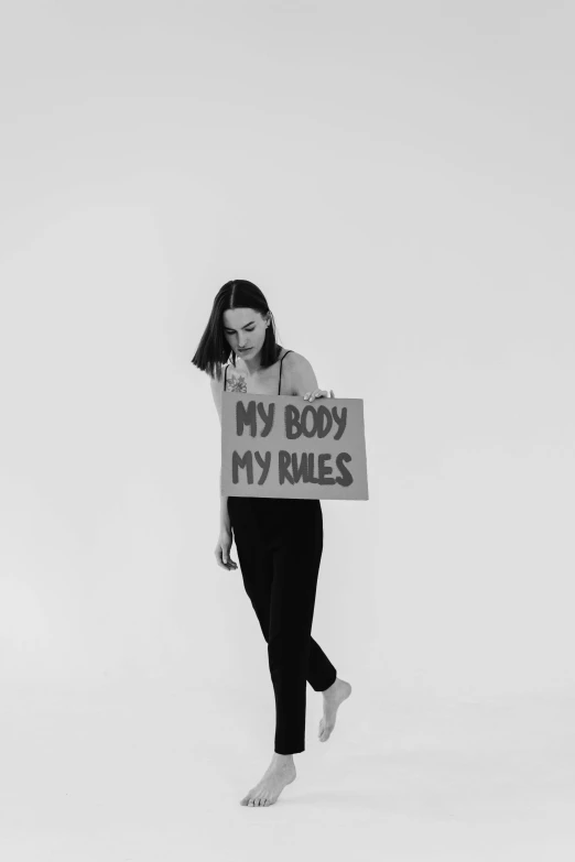 a black and white photo of a woman holding a sign, an album cover, inspired by Vanessa Beecroft, tumblr, antipodeans, body fit, rule, body meshes, trans rights