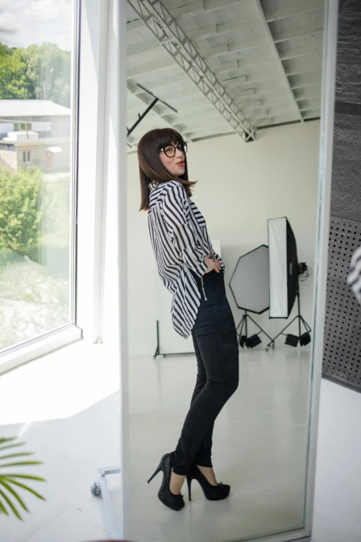 a woman standing in front of a mirror in a room, wearing stripe shirt, modeling studio, black jeans, gemma chen