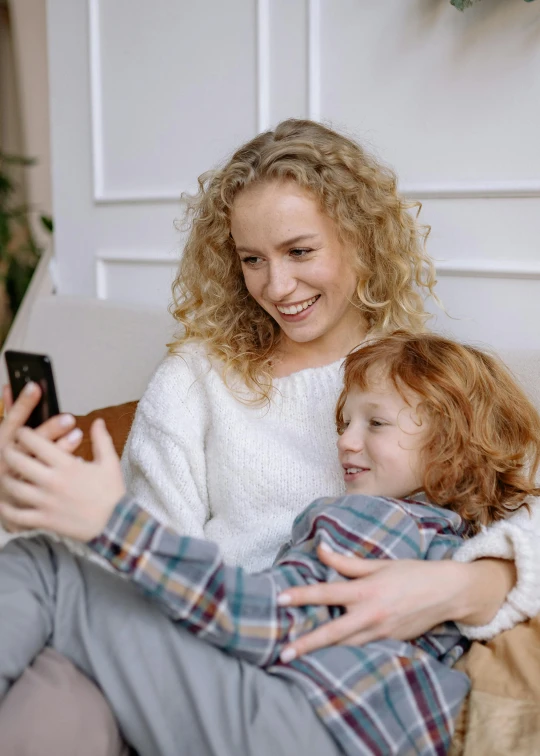 a woman sitting on top of a couch next to a child, a picture, pexels, incoherents, 8k selfie photograph, curly blond, gif, phone camera