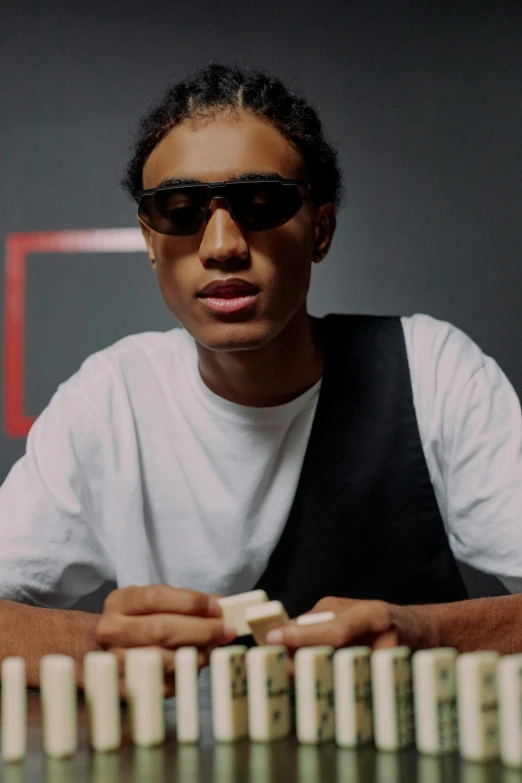 a man sitting at a table with dominos in front of him, an album cover, trending on unsplash, hyperrealism, ashteroth, poker face, black teenage boy, wearing oakley sunglasses