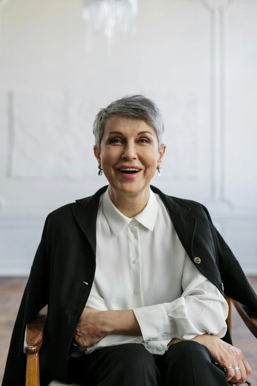 a woman sitting in a chair in a room, a character portrait, trending on pexels, short silver hair, very happy, lawyer, androgynous