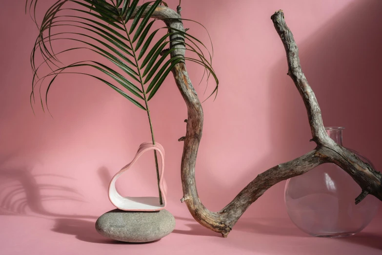 a vase sitting on top of a table next to a tree branch, an abstract sculpture, inspired by Isamu Noguchi, pink arches, rose gold heart, serpentine pose, tropical atmosphere