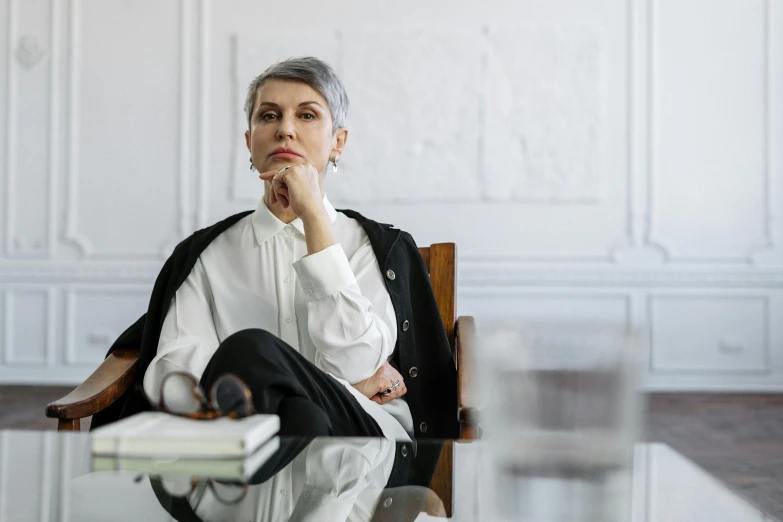 a woman sitting at a table with her hand on her chin, pexels, hyperrealism, short silver hair, office clothes, sitting on designer chair, lawyer