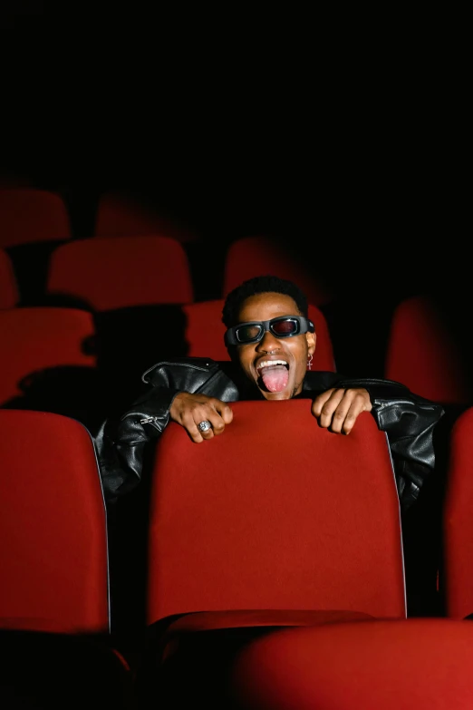 a man sitting on top of a red chair in a movie theater, ray lewis yelling, highly upvoted, wearing 3 d glasses, [ theatrical ]