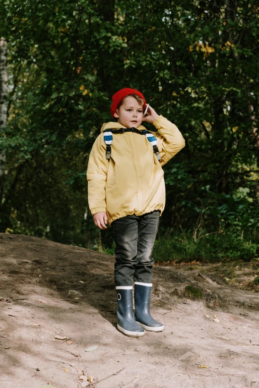 a little boy standing on a dirt road talking on a cell phone, by Grytė Pintukaitė, pexels, yellow raincoat, full body with costume, greta thunberg, standing in a pond