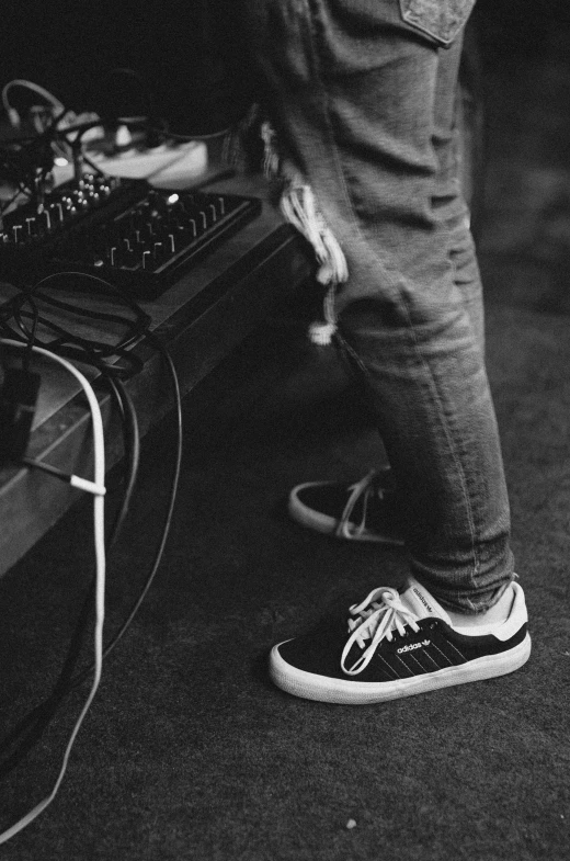 a person standing in front of a dj's equipment, a black and white photo, unsplash, realism, wearing white sneakers, guitarist, wearing adidas clothing, featuring wires