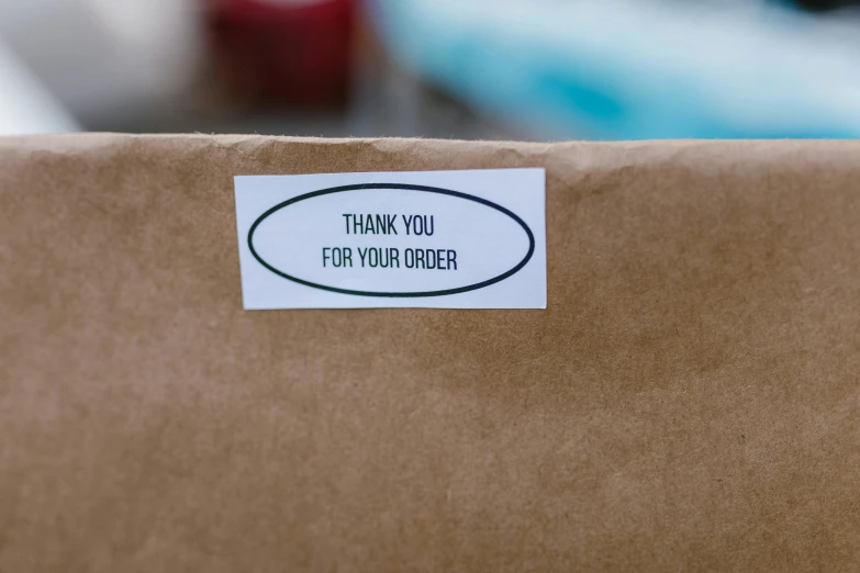 a brown box with a sticker that says thank you for your order, by Daniel Lieske, pexels contest winner, shot on 1 5 0 mm, conor walton, thumbnail, foil