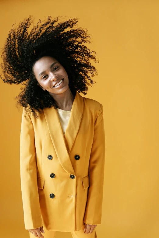 a woman standing in front of a yellow background, trending on pexels, wearing wool suit, curls, happy girl, wearing a fancy jacket