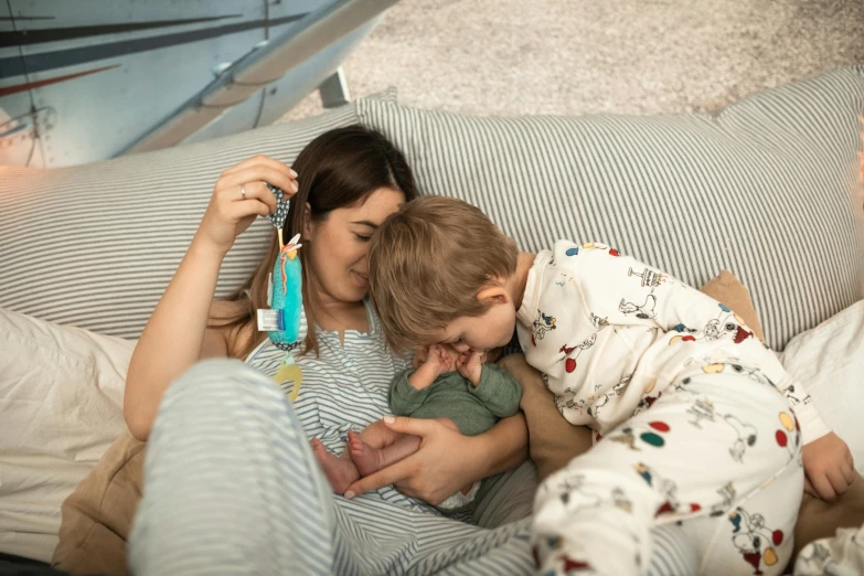 a woman and two children laying on a bed, pexels contest winner, cuddling her gremlings, the birth, nursing, gray