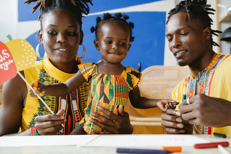 a couple of people that are sitting at a table, by Ingrida Kadaka, pexels contest winner, black arts movement, with a kid, sharpie, lady using yellow dress, yoruba body paint