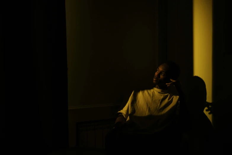 a man sitting in a chair in a dark room, inspired by Elsa Bleda, pexels contest winner, realism, dark skin, yellow light, silhouette :7, medium format. soft light