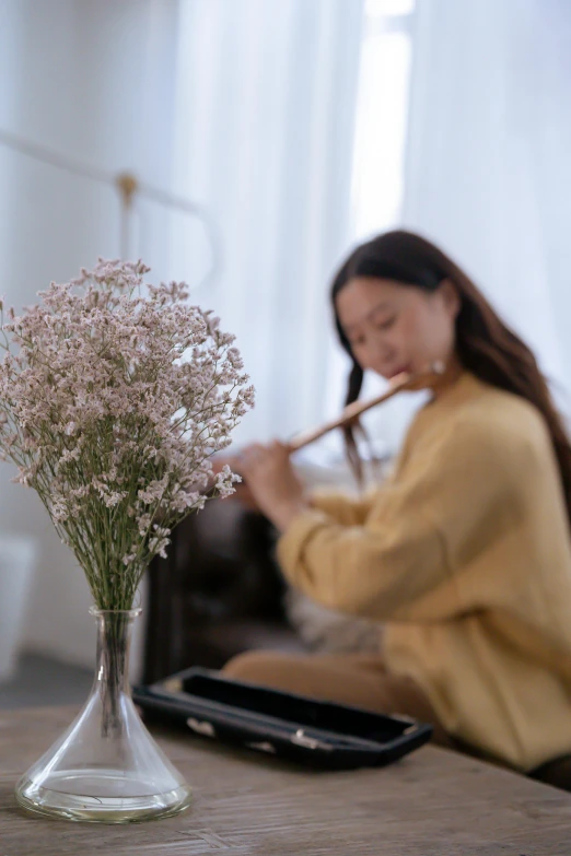 a woman sitting on a couch playing a flute, inspired by Song Xu, trending on pexels, made of dried flowers, gypsophila, sweeping, at home