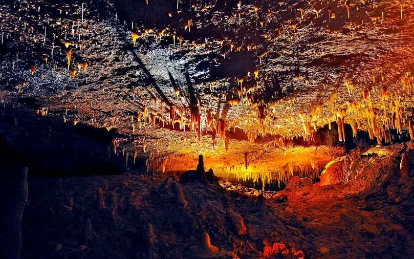 a group of people standing inside of a cave, orange neon backlighting, high detailed thin stalagmites, promo image, panorama