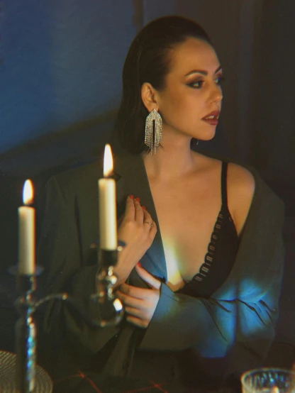 a woman sitting at a table with a candle, an album cover, inspired by Elsa Bleda, trending on pexels, renaissance, huge earrings, generous cleavage open jacket, dark. studio lighting, (night)