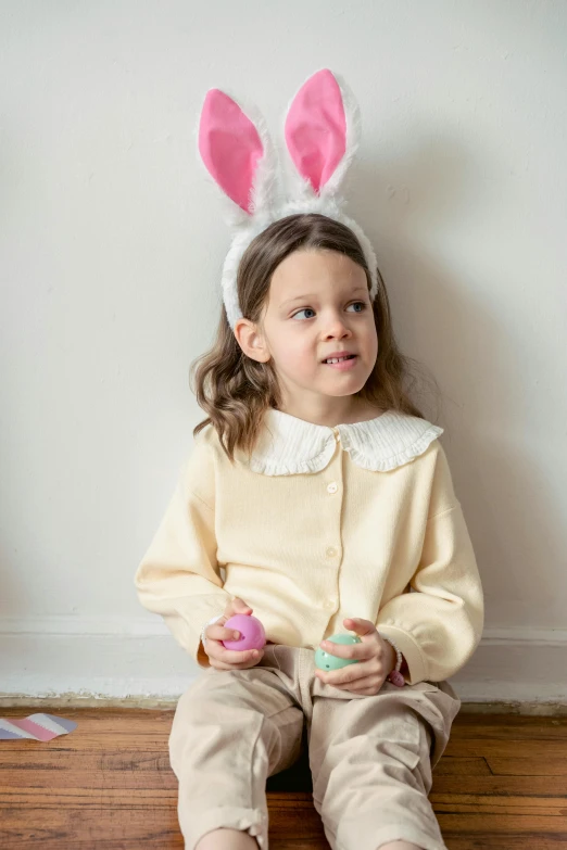 a little girl wearing bunny ears sitting on the floor, a portrait, inspired by Elsa Beskow, pexels, holding easter eggs, collared shirt, frown fashion model, loose - fitting blouses