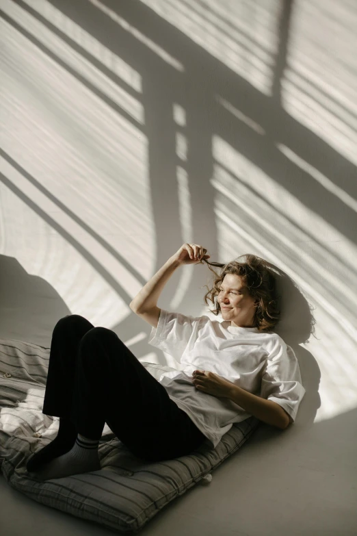 a woman sitting on top of a bed next to a window, pexels contest winner, light and space, wearing a white shirt, excellent light and shadows, curly haired, sun beaming down on him