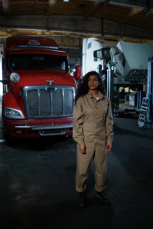a woman standing in front of a red truck, a portrait, by Dan Frazier, renaissance, technical suit, in a workshop, promo image, an olive skinned