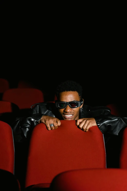 a man sitting in the middle of a row of red chairs, an album cover, pexels, wearing 3 d glasses, movie clip, black man, [ theatrical ]