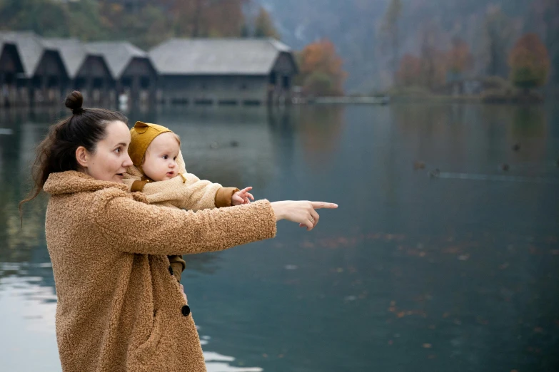 a woman holding a baby near a body of water, pointing, fall, guide, sound of music