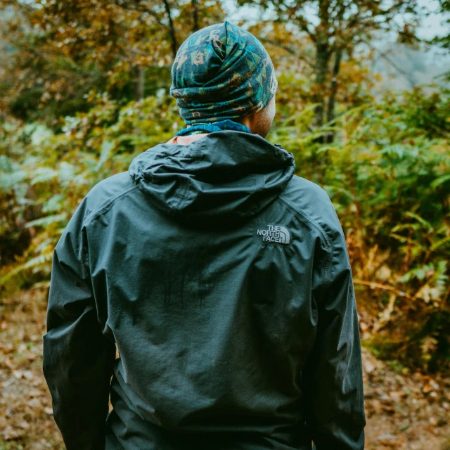 a man standing in the woods with his back to the camera, a picture, hat and hoodie, high quality product image”, raining outside, wearing jacket