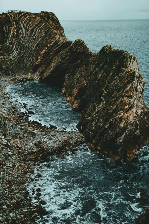 a rocky beach next to a body of water, an album cover, pexels contest winner, romanticism, geological strata, ((rocks)), steep cliffs, telephoto long distance shot