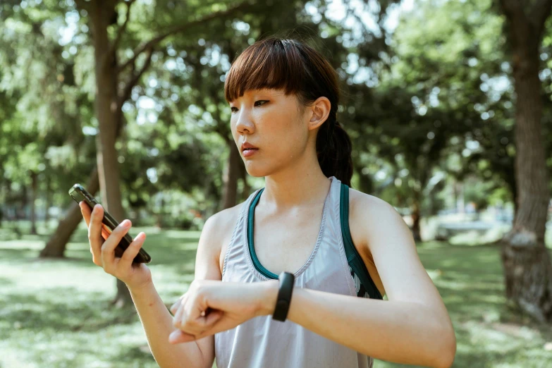 a woman standing in a park looking at her cell phone, trending on pexels, of taiwanese girl with tattoos, wearing fitness gear, avatar image, wearing a watch