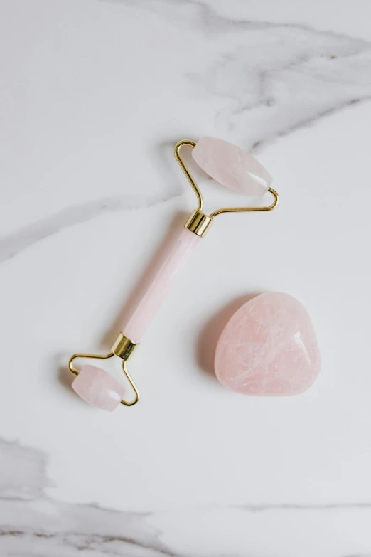 a rose quartz roller on top of a marble counter, inspired by Hedi Xandt, reddit, heart shaped face, limbs, flat lay, gold