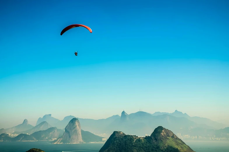 a paraglider flying over the ocean with mountains in the background, by Felipe Seade, pexels contest winner, rio de janeiro, avatar image, 9 9 designs, wide high angle view