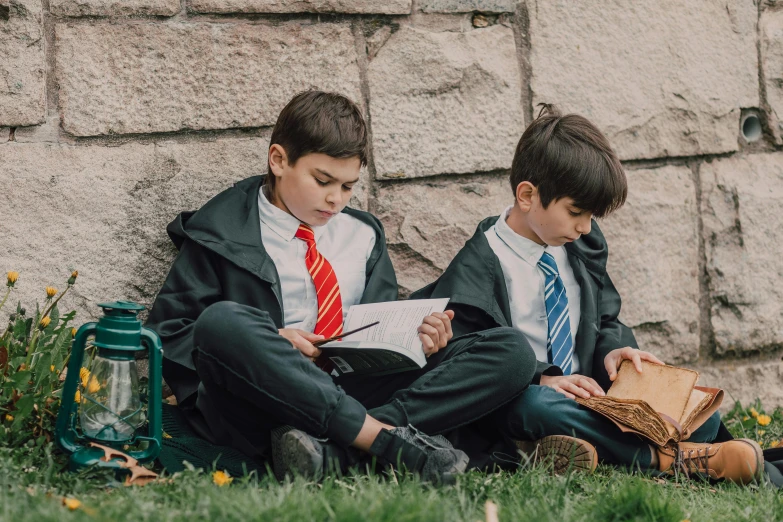 a couple of young boys sitting on top of a grass covered field, an album cover, pexels contest winner, heidelberg school, magical school student uniform, reading a book, hogwarts legacy, bowater charlie and brom gerald