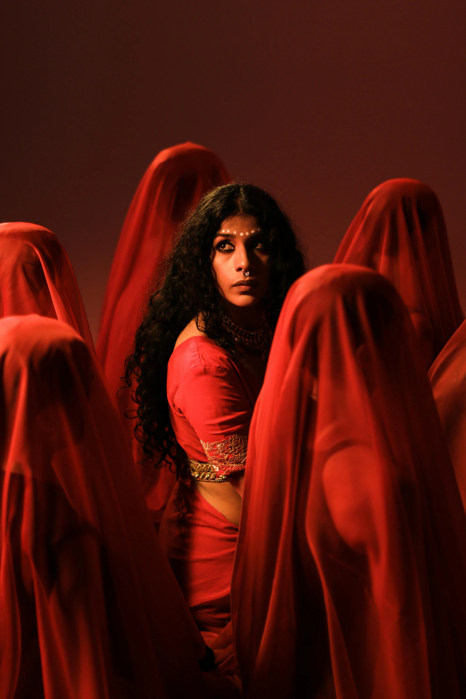 a woman in a red dress surrounded by red cloths, staring, provocative indian, [ theatrical ], sza