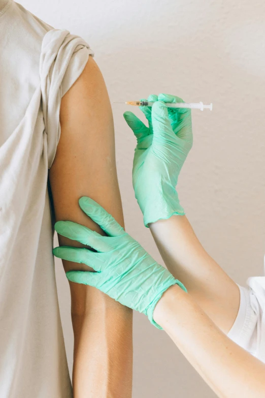 a person in a white shirt and green gloves, a colorized photo, shutterstock, iv pole, from the elbow, holding syringe, woman holding another woman