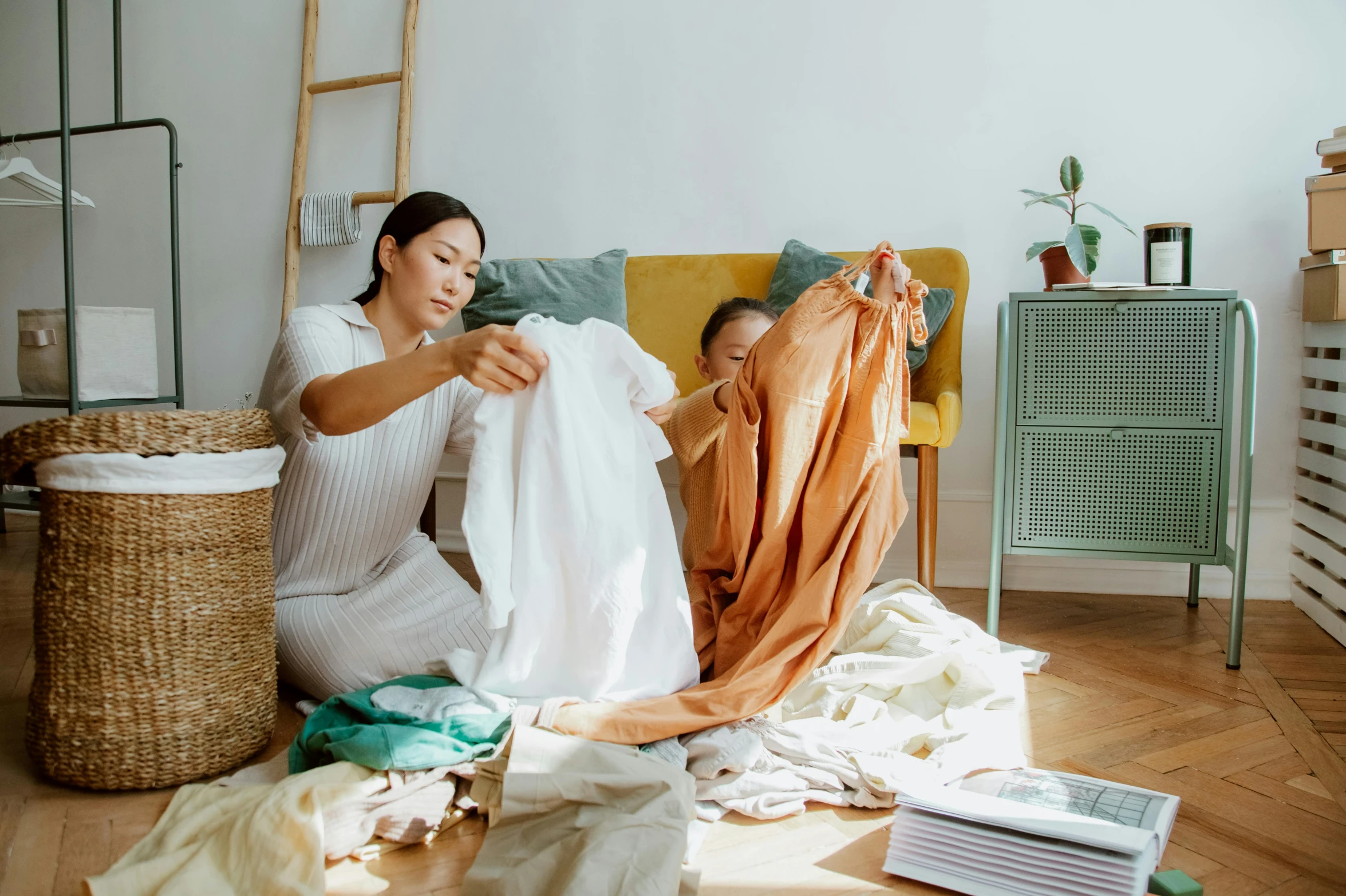 a woman sitting on the floor next to a pile of clothes, by Julia Pishtar, pexels contest winner, happening, husband wife and son, flowing fabric, inspect in inventory image, asian woman