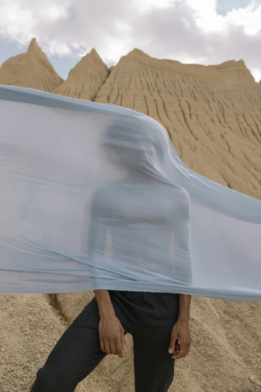 a man standing in front of a mountain covered in a sheet, a surrealist sculpture, inspired by Anna Füssli, unsplash, girl walking between dunes, blue gray, made of fabric, ultrafine detail ”