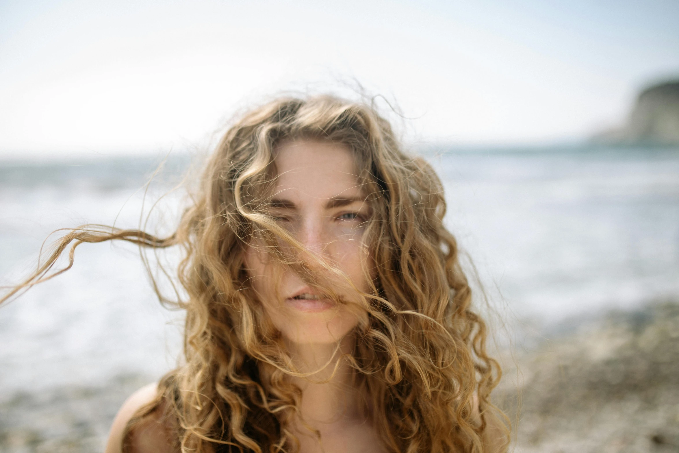 a woman standing on top of a beach next to the ocean, by Carey Morris, pexels contest winner, renaissance, messy hair bedhead, close up portrait of woman, permed hair, unsplash transparent