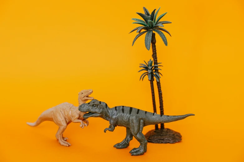 a couple of toy dinosaurs standing next to each other, inspired by Adam Rex, pexels contest winner, a palm tree, eating, gray and orange colours, ray harryhausen