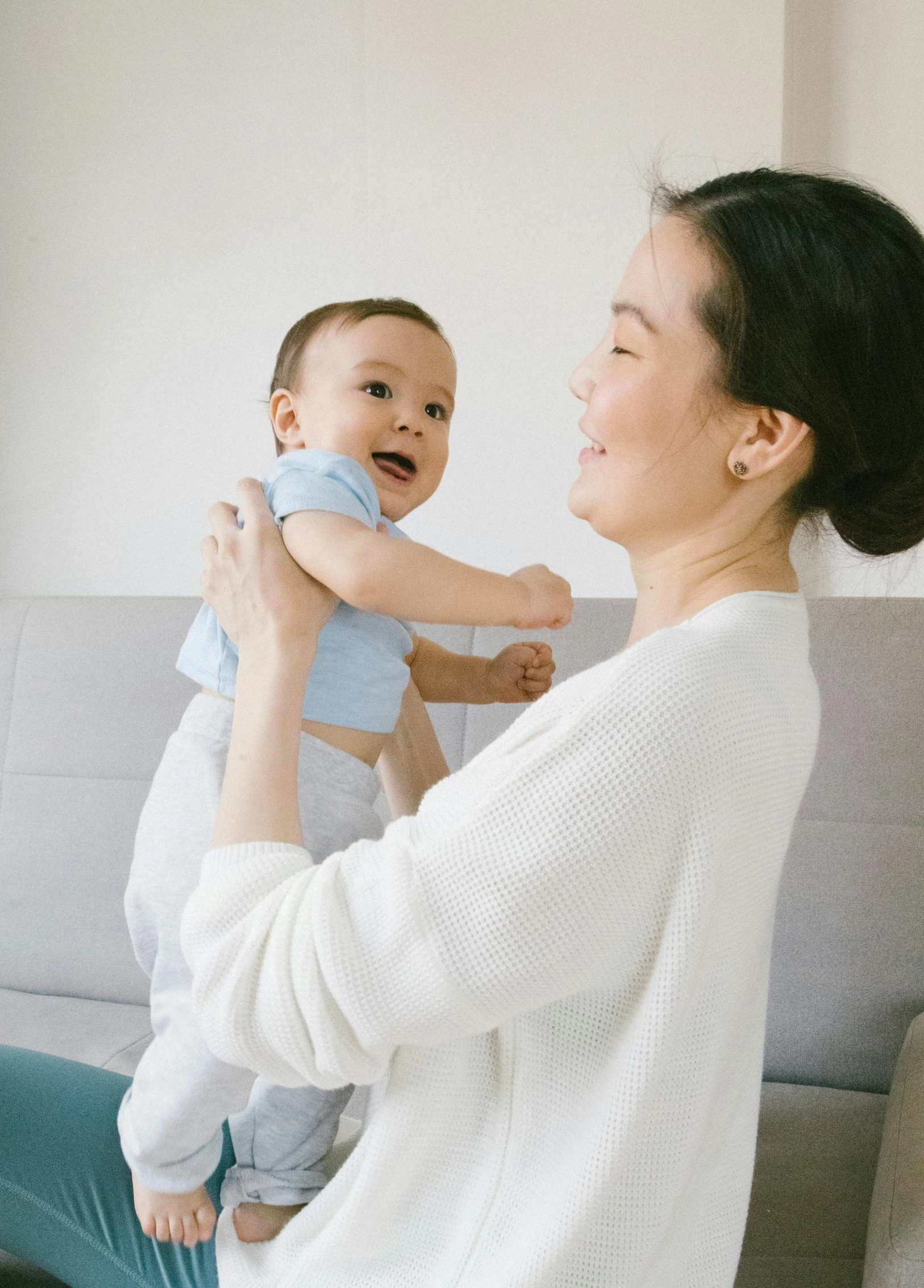 a woman sitting on a couch holding a baby, pexels contest winner, happening, wearing a light blue shirt, standing sideways, asian male, thumbnail