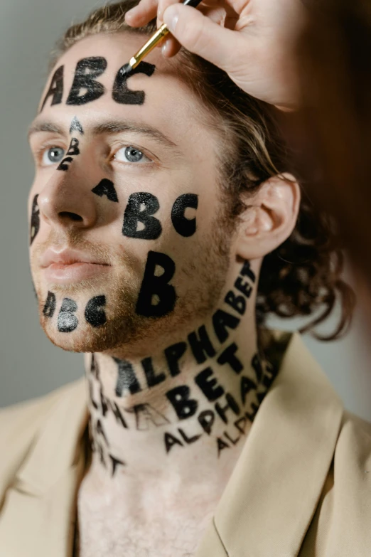 a man with letters painted on his face, by Adam Marczyński, trending on pexels, art & language, timothee chalamet, abcdefghijklmnopqrstuvwxyz, face and body clearly visible, acne