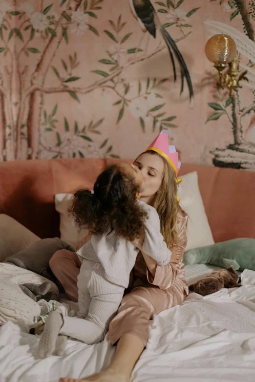 a woman sitting on top of a bed next to a little girl, wearing a party hat, kissing each other, manuka, tv commercial