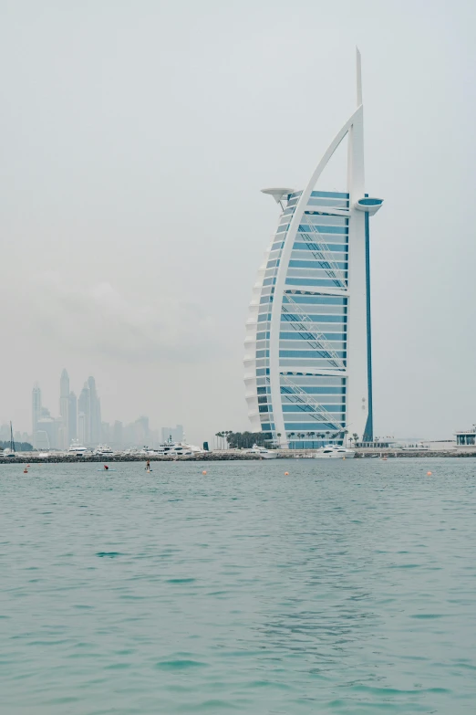 a view of the burj al arab hotel from the water, hazy water, distant cityscape, grey sky, stacked image