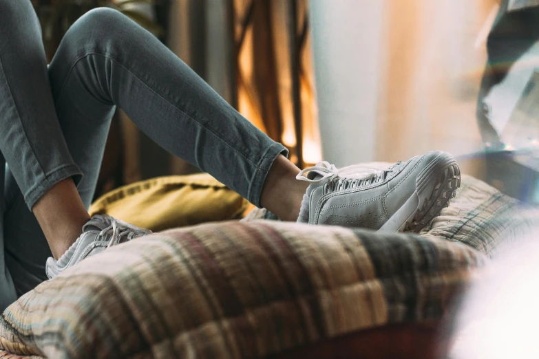 a person laying on a bed with their feet on a pillow, inspired by Sarah Lucas, trending on pexels, happening, blue jeans and grey sneakers, sitting on an armchair, teenage girl, afternoon hangout