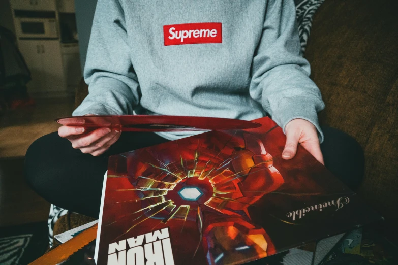 a person sitting on a couch holding a book, an album cover, inspired by Raymond Han, unsplash, nuclear art, supreme pizza, superior iron man, low quality photo, trending on r/streetwear