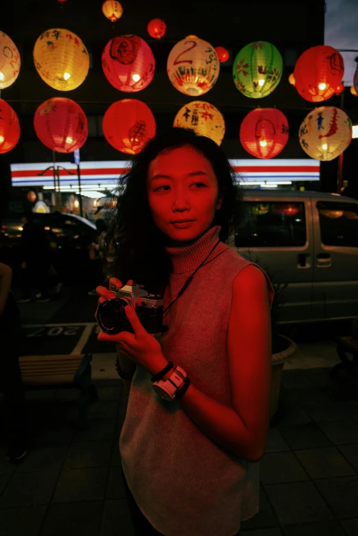 a woman standing in front of a building holding a camera, a picture, by Reuben Tam, reddit, with paper lanterns, awards, taken in night club, holding origami qilin