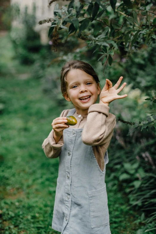 a little girl that is standing in the grass, pexels, holding an avocado in his hand, wearing farm clothes, excited, an apple